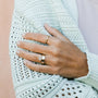 A person in a light blue knit sweater displays two Simple Stud Rings—18k gold plated with geometric designs—on their fingers. Their short, natural nails are shown against a soft peach-colored wall.