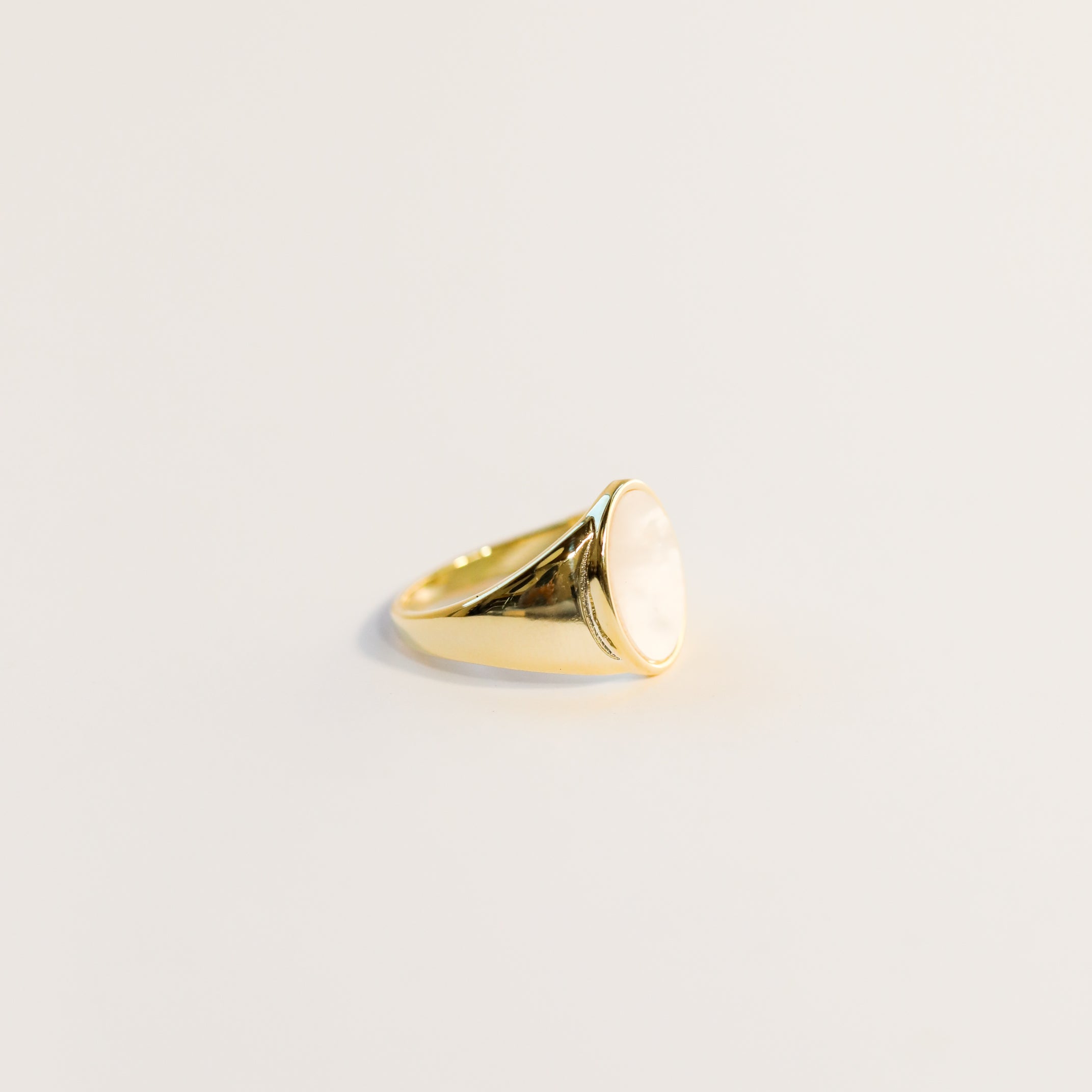 The Mother of Pearl Signet Ring showcases a smooth, oval mother of pearl stone set atop a gold band, displayed on a plain light background.
