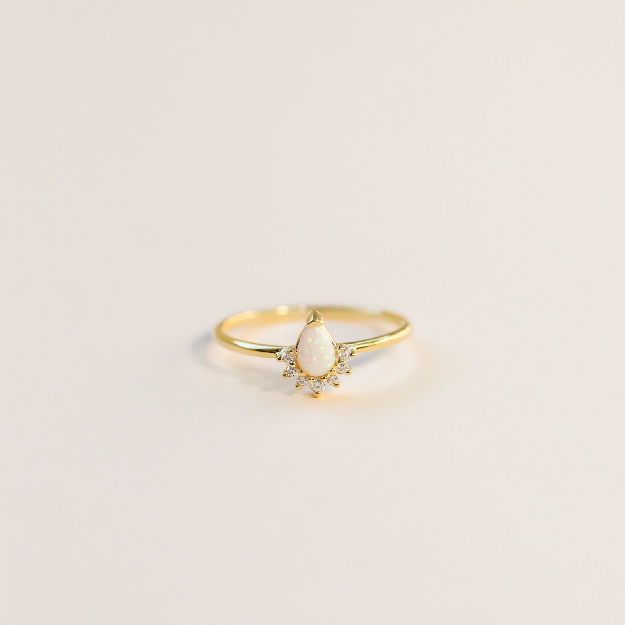 The Opal Burst Ring features a delicate 18k gold-plated band with a teardrop-shaped lab-grown Opal center and small round accent stones, shown on a plain light background.