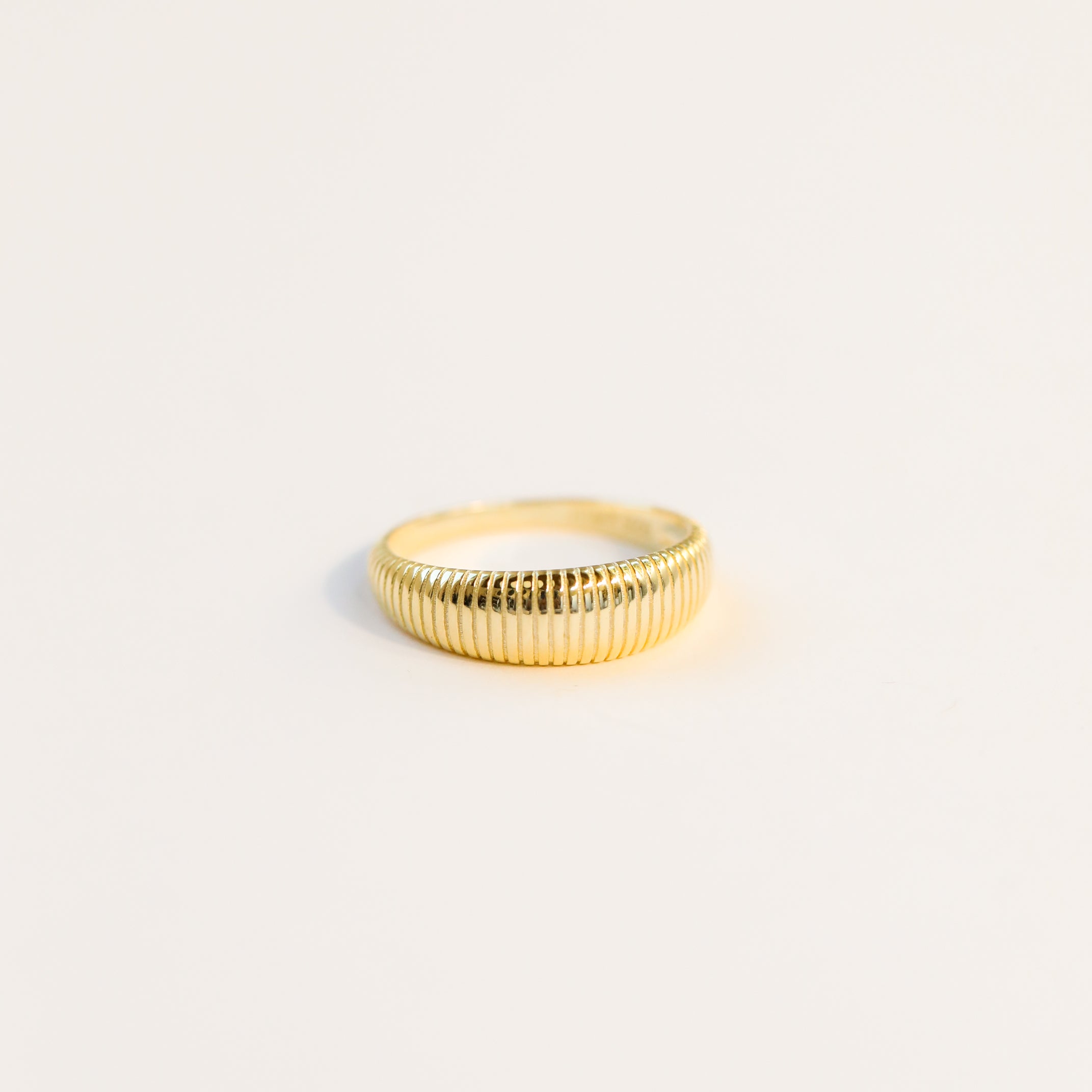 The Ridged Ring, featuring a ridged textured design and 18k gold plating, is displayed against a simple, light background.