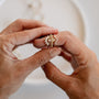 Close-up of two hands holding the Lambda Ring set: a gold-plated floral design ring paired with a v-shaped band, shown against a soft, blurred background.
