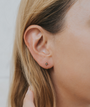 Close-up of a woman's ear adorned with the Star Huggie and a gold sunburst stud earring featuring a clear gemstone center. Her blond hair is tucked back as a hand gently touches it, set against a softly blurred background.