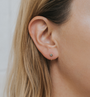 Close-up of a woman's ear wearing the Sun Huggie—small gold earrings shaped like a sun with a green center. Her light brown hair and fair skin complement these delicate earrings, adding a radiant touch to her look.