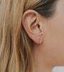 Close-up of a woman's ear with straight blonde hair, wearing the Minimalist Horseshoe—an 18k gold-plated earring shaped like a delicate, curved bar.