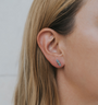 Close-up of a person’s ear with straight, light brown hair, wearing the Amazonite Mineral Point - Hope earring—a small, polished amazonite gemstone set on sterling silver posts. The background is a plain, light-colored surface.