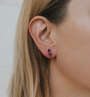 Close-up of a person with light skin and straight blonde hair wearing an Amethyst Mineral Point - Healing earring, featuring a small, dark purple rectangular gemstone stud and sterling silver posts. The background is blurred.
