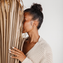 A woman with curly hair in a bun, wearing a cream knit sweater and Silver Swirl Hoop earrings, stands sideways, partially hiding her face behind tall dried palm leaves against a neutral background.