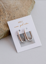 The Silver Rectangle Hoop - Large earrings are displayed on a white jewelry card with gold “JaxKelly wear good vibes” text, next to beige stone on a light gray surface.