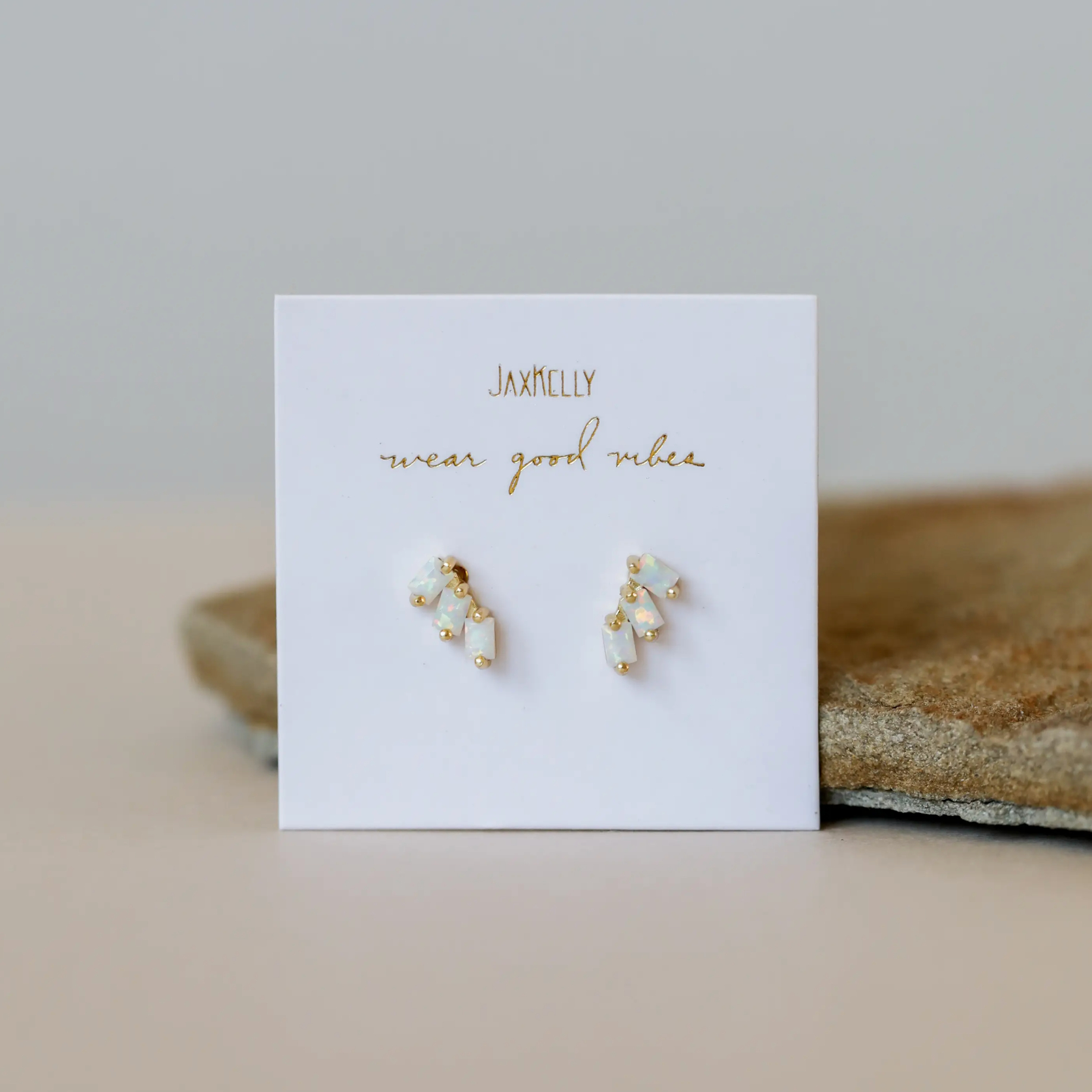 The Offset Trio - White Opal features small, gold plated stud earrings with lab-grown white opal, displayed on a white JaxKelly card reading "wear good vibes" in gold script, set against a neutral background.