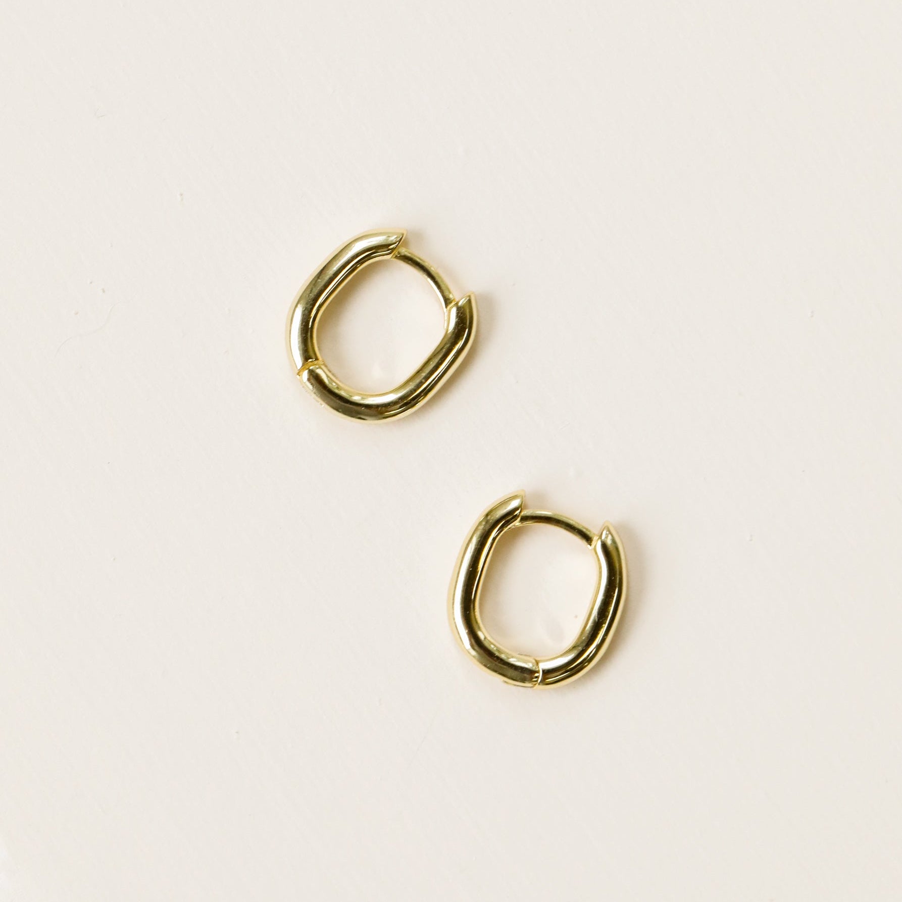 The Small Rectangular Hoop earrings feature chunky, slightly squared gold rectangles with sterling silver posts and radiant gold plating, resting on a plain, light-colored surface.