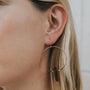 Close-up of a woman's ear wearing the Smoky Quartz Hoop - Protection: a handcrafted gold hoop earring with a black vertical bar pendant, her blonde hair tucked back against a neutral background that highlights the design.