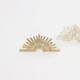 A gold Sunburst Stud earring features fan-shaped rays with tiny sparkling crystals in radiating lines, while another similar gold vermeil Sunburst Stud is blurred in the background on a white surface.
