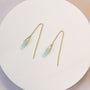 The JaxKelly Gemstone Threader - Amazonite features gold plated threader earrings with light blue amazonite pendants, elegantly displayed on a round white surface.