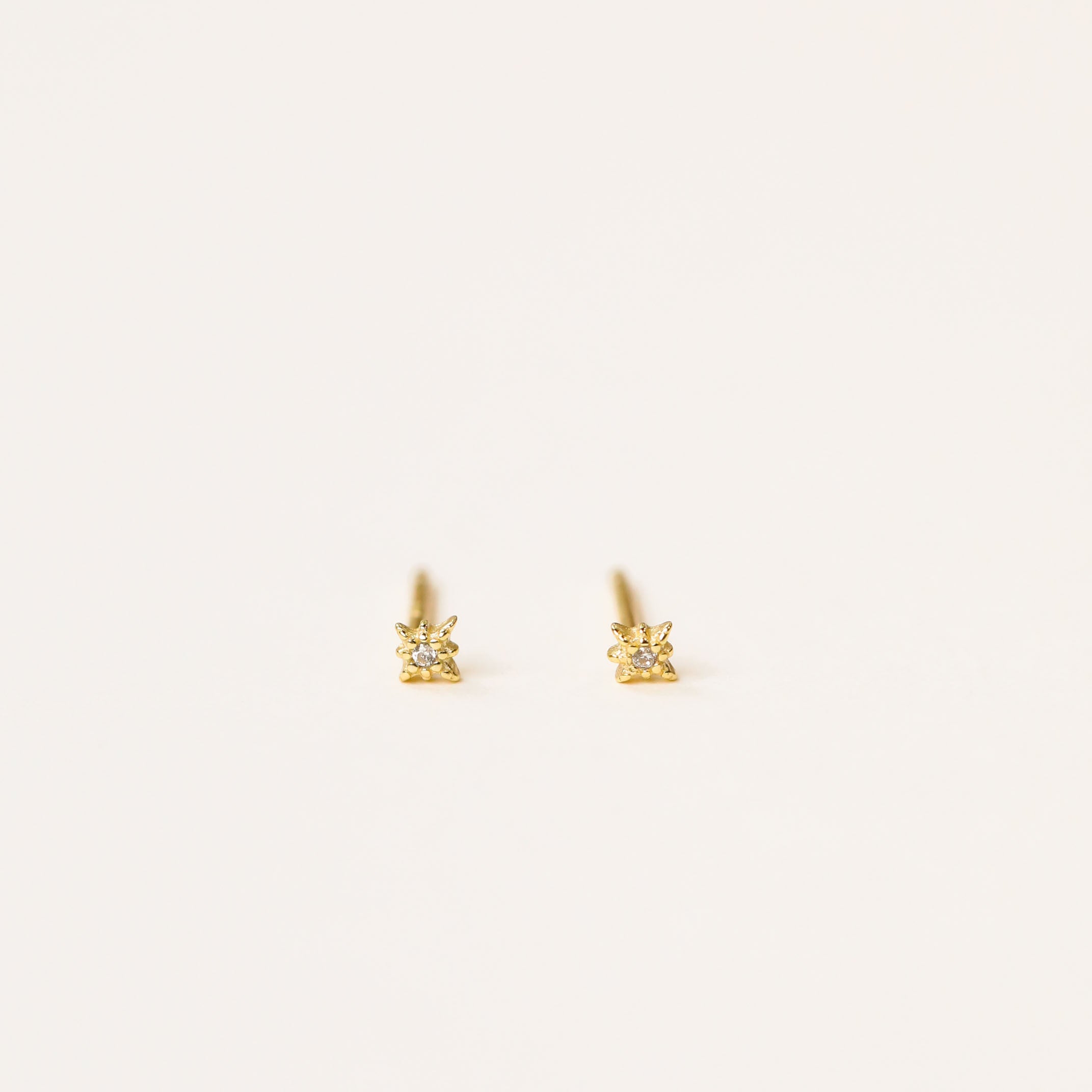 The Tiny Star earrings are mini stud earrings featuring single clear gemstones, an 18k gold plated finish, and sterling silver posts, shown against a plain white background.