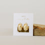 The Gold Wide Hoop earrings feature a shiny 18k gold-plated finish, displayed on a white card with gold text, set against a neutral background with a beige stone beside them.