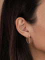 A close-up of a woman's ear with straight dark brown hair, wearing the Large Ball Hoop— a gold plated earring featuring a beaded texture and sterling silver posts.