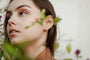 A young woman with brown hair gazes to the side, framed by green leaves. She wears a light brown shirt and Pavé Silver Hoops, which add an elegant sparkle against the neutral background.