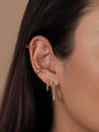 Close-up of a woman's ear adorned with the Large Ball Hoop and other gold earrings, some with sterling silver posts for comfort. Her straight brown hair is tucked behind her ear against a neutral background.