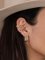 Close-up of a woman's ear with dark hair in a light-colored hat, styled with multiple 18k gold plated earrings featuring the Cross Stud and other hoops and studs. All earrings have sterling silver posts.