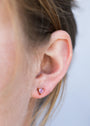 Close-up of a person's ear with light brown hair, wearing Amethyst Mini Energy Gems - Healing: small, triangular light purple studs set in 18k gold plating with sterling silver posts.