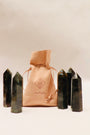 A peach-colored JaxKelly drawstring pouch is surrounded by five upright, dark Labradorite Crystal Points, polished and believed to enhance a protective aura, all displayed on a light background.